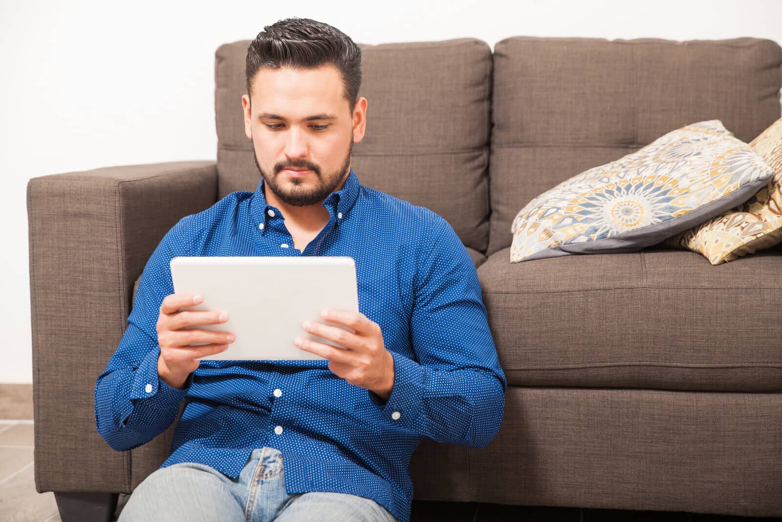 Man Sitting in Front of Couch Looking at Tablet