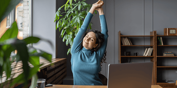 Happy Employee Stretching Arms at Desk Knowing How to Improve Employee Morale